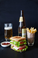 sandwich with beer and french fries on a black background