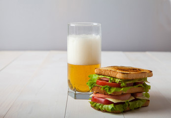 sandwich and a glass of beer on a  white wooden table