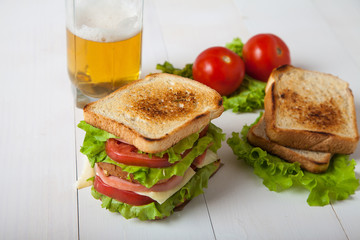 sandwich, tomato, toast, salad and glass with beer on white wood