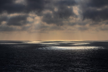 Dunkle Wolken lassen einzelne Lichtspots auf den Ozean strahlen