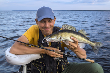 Happy fisherman with zander fish trophy at the boat with fishing tackles