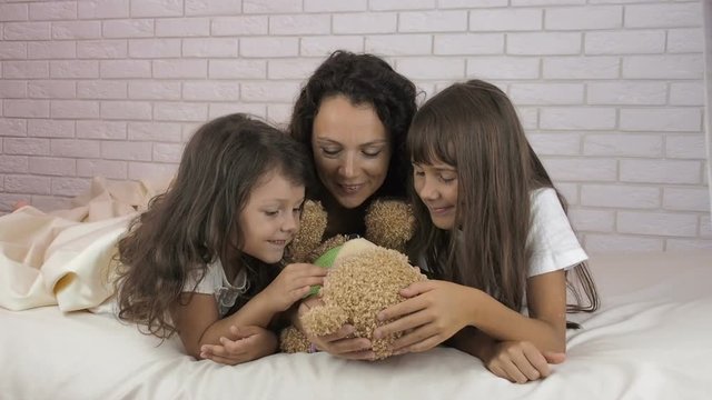 Happy family in the bedroom. Mother with daughters and a bear on the bed.
