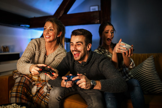Group of best friends sitting at home on pleasant evening and playing games on console.They challenge each other to win .