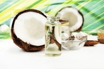 Coconut oil in bottle with open nuts and pulp in jar, green palm leaf background. Natural cosmetic...