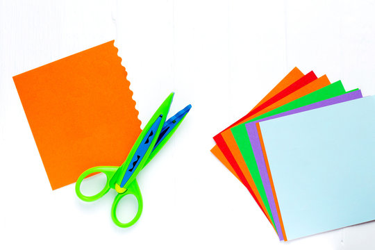 Color paper for origami is a fan, scissors with a wavy edge. On white table