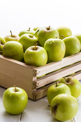 Green apples in crate close up on white background with selective focus on apple with water droplets