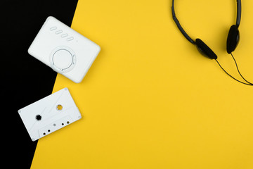 top view of a white audio cassette tape and a white portable cassette player with a black headphone...