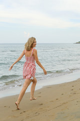 happy young woman is running along seashore, wearing short red checked dress