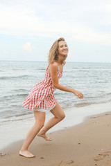 young woman is running along seashore, wearing short red checked dress