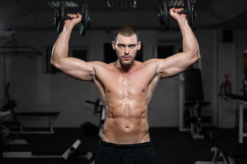 Fototapeta na wymiar Muscular man in the gym training with dumbbells, guy pumps his deltoid muscle