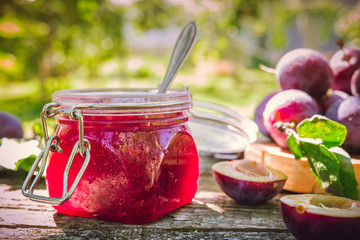 Glass jar with plum jam confiture and ripe plum berries in a basket on a wooden vintage table in the garden with a copy space, the idea of home canning and organic ecological bio nutrition © shintartanya