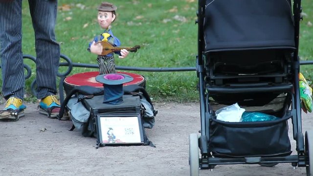 Street puppet show. Doll of a musician perfoms music to the kids in a park.
