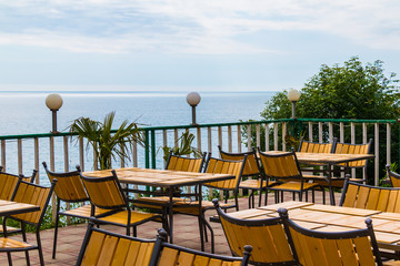 Terrace with wooden tables and chairs with sea view in sunny summer day
