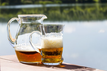 Pitcher with a mug of fresh beer on the table by the lake