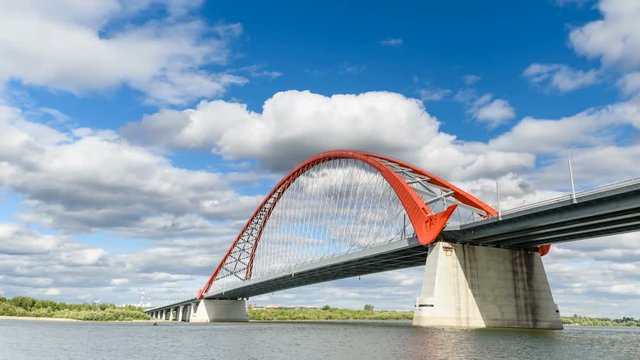Clouds are running in the blue sky over the red bridge over the Ob river. Timlaps, Novosibirsk, Siberia.
