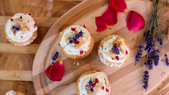 Flat lay of beautiful cupcakes on platter with edible flower decoration lavender and rose petals