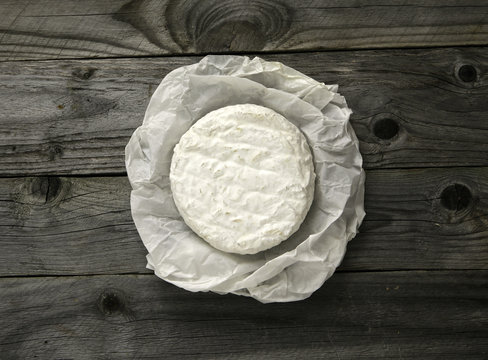 Ripe tasty cheese camembert or brie wrapped in a paper on an old plank table