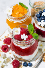 desserts with muesli, berry and fruit puree in jars on white table, top view closeup