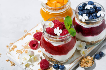 desserts with muesli, berry and fruit puree in jars on white table, top view