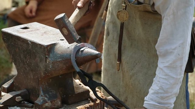 Blacksmith work. Blacksmith beats a piece of hot metal with a hammer on an anvil. The smith forges a horse horseshoe.