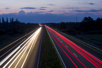 Speedway at night, car lights and road with sky and clouds.