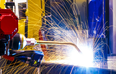 industrial yellow robot welder close - up conduct welding of metal parts, metal droplets are...