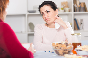 Unhappy female talking with mother at table