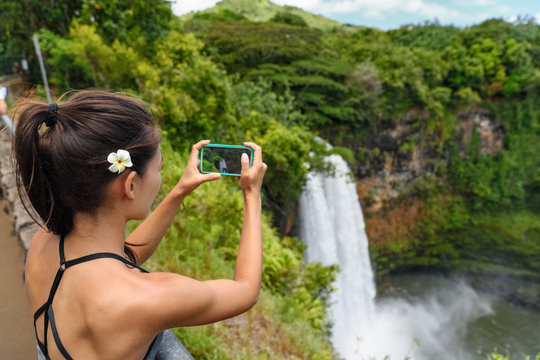 Tourist taking photo pictures of Akaka Falls waterfall on Hawaii, Big Island, USA. Travel tourism concept with multicultural tourist couple.