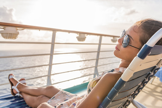 Cruise ship vacation woman relaxing lying on deck lounger at sunset casual lifestyle. Girl enjoying sunshine laid back sleeping on balcony chair on travel summer holidays.
