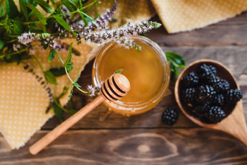 Honey in jar, honey dipper, flowering mint and blackberries on a wooden table. View from above.