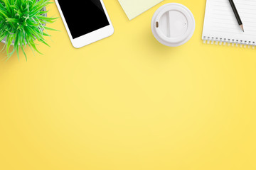 Yellow office desk composition with mobile phone, plant, coffee, notepad and pen. Flat lay.