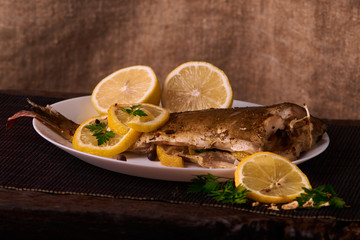 delicious roasted carp fish with lemon slices, spices, and fresh rosemary on white plate, view from above, close-up