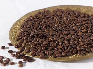 Kaffeebohnen auf goldenem Teller und weißer Tischdecke