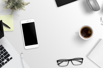 Office desk composition with mobile phone with blank screen for mockup. Copy space in the middle. Flat lay.