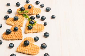 Traditional belgian waffles form of heart with fresh blueberry and sweet cherry on white wooden background. Flat lay, top view, copy space.
