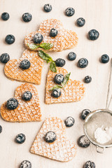 Traditional belgian waffles form of heart with fresh blueberry and sweet cherry on white wooden background. Flat lay, top view, copy space.