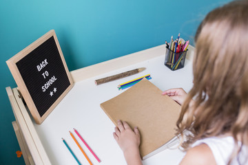 young kid girl working on her desk and doing homework or drawing. Letter Board on table with back to school words. Concept