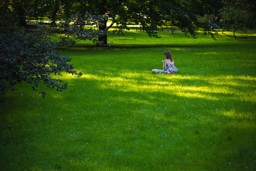 soft focus girl sit on grass in green garden nature environment back to camera and looking at phone