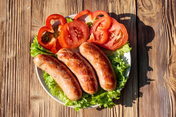 Grilled sausages with fresh vegetables on wooden table