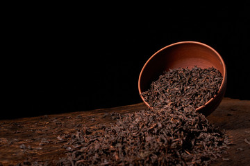 Dry tea leaves in clay bowl on black background. selective focus