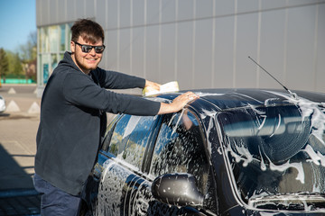 young man in sunglasses washing car at self service carwash