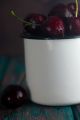 Cherries in tin cup on rustic wooden desk.