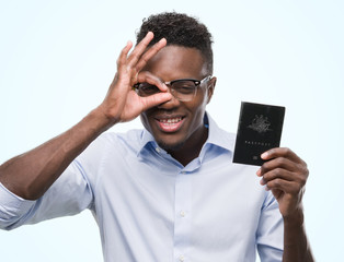 Young african american man holding australian passport with happy face smiling doing ok sign with hand on eye looking through fingers