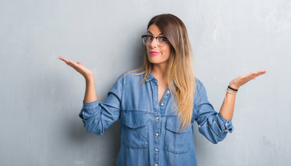 Young adult woman over grunge grey wall wearing glasses clueless and confused expression with arms...