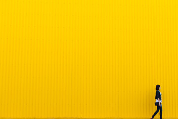 Woman walking near yellow wall, copy space background