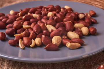 Peanut snacks nuts eating snacks red peanuts peanuts fried peanuts on blue plate on sackcloth. selective focus