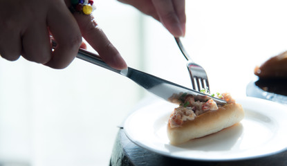 Asian woman hands are cutting a piece of canape with knife and fork while enjoy afternoon tea or high tea. Natural lighting.