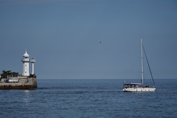 Fototapeta na wymiar View of the lighthouse in the sea and a floating white yacht.