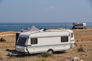 The house on wheels is parked on the beach in front of the blue sea in the wild among the cars.