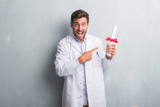 Handsome Young Doctor Man Over Grey Grunge Wall Holding Diploma Very Happy Pointing With Hand And Finger